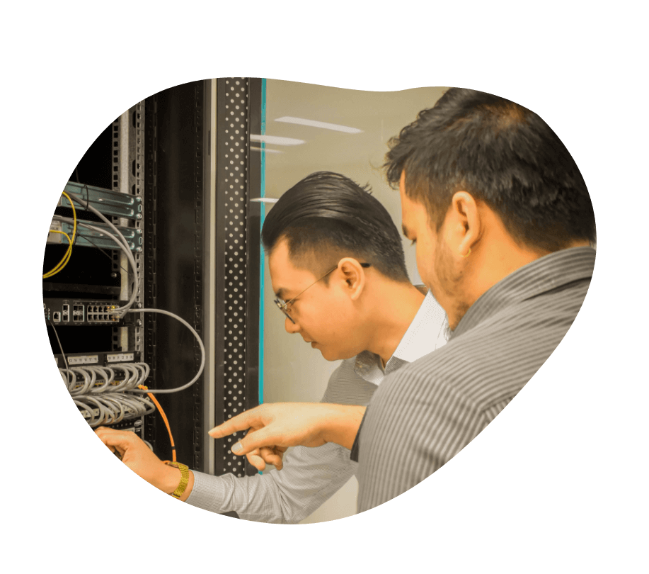 Two TRT employees stand in front of a server rack, examining wires and equipment for maintenance and troubleshooting.