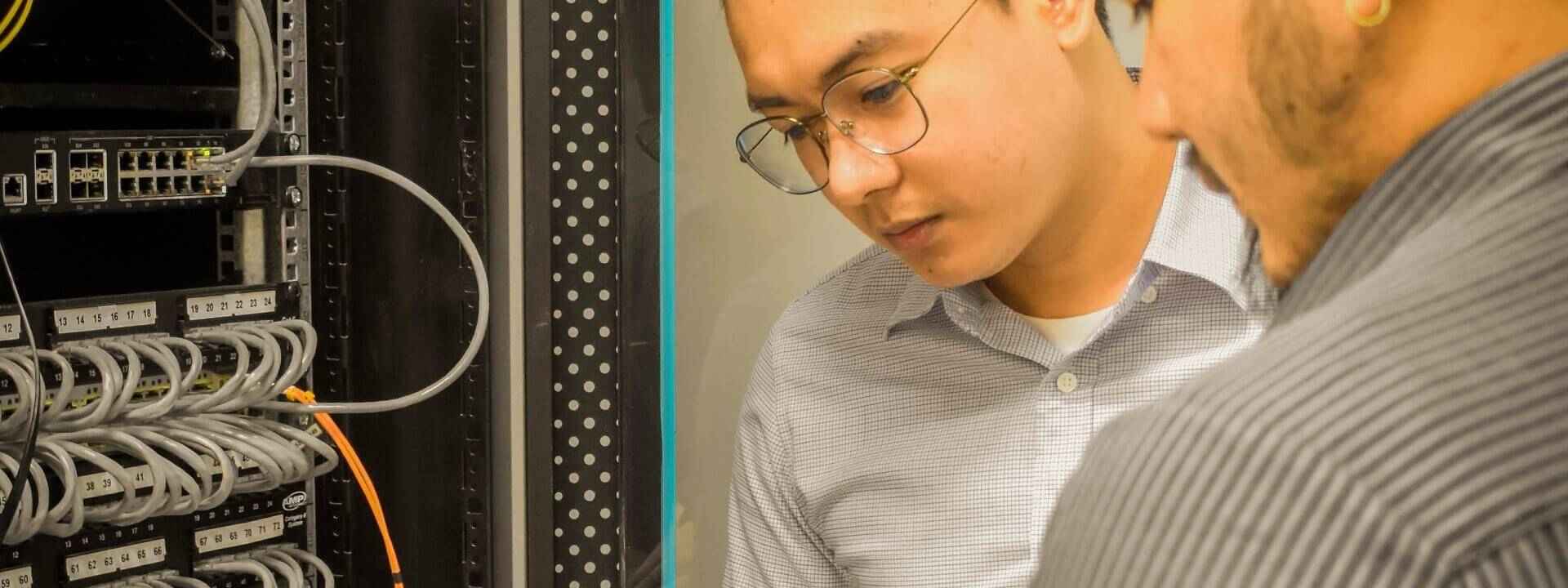IT professionals inspecting server rack, monitoring network cables and hardware for optimal performance in a data center environment. Practical IT Strategies