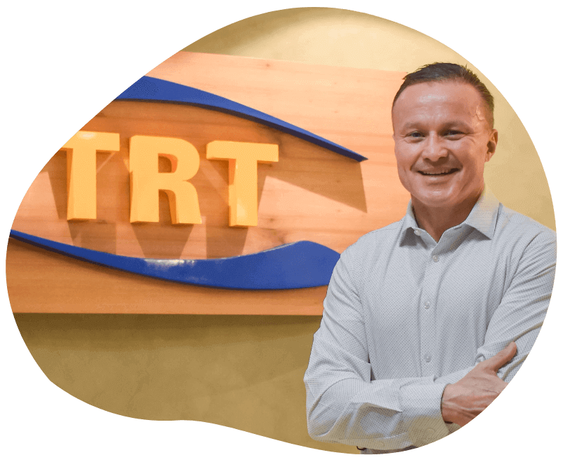 A man stands confidently in front of a TRT sign, representing Domenic Romanelli, CEO of Total RISC Technology.