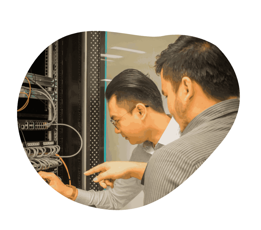 Two TRT employees stand in front of a server rack, examining wires and equipment for maintenance and troubleshooting.